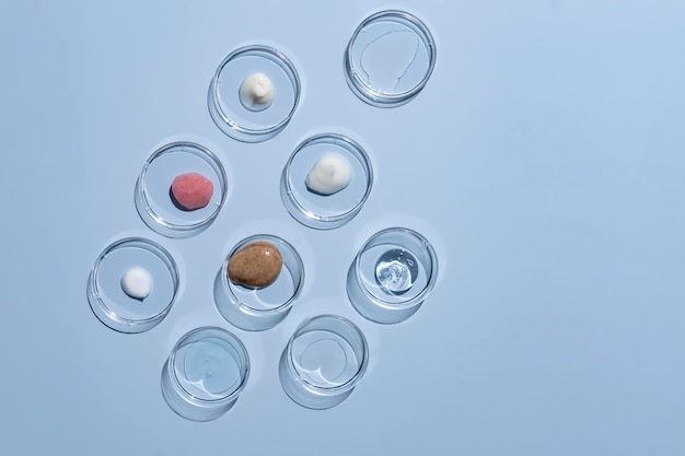 Mehrfarbige Texturen aus Creme-Peeling-Serum und Öl in Petrischalen auf blauem Hintergrund Konzept der Kosmetiklaborforschung Hautpflegekosmetik Produktproben Wellness- und Schönheitskonzept