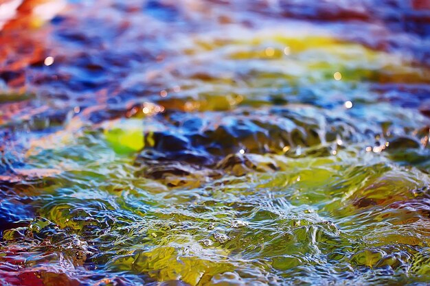 mehrfarbige Texturoberfläche des Wasserstroms, klares Wasser, farbige Steine am Grund des Flusses