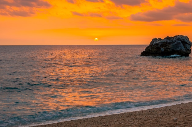 Mehrfarbiger Sonnenaufgang über ruhigem Wasser. Sandstrandstreifen an der griechischen Mittelmeerküste