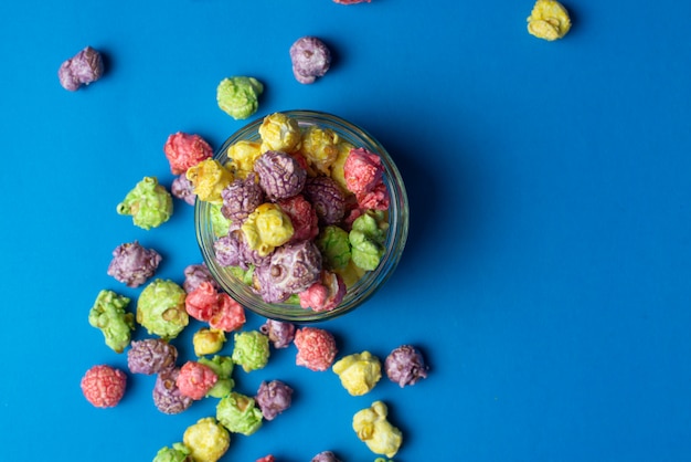 Mehrfarbiges Popcorn mit Fruchtgeschmack in Glasbechern auf blauem Hintergrund. Popcorn mit Bonbonüberzug.