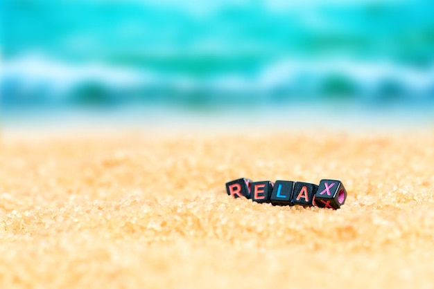 Foto mehrfarbiges wort relax aus schwarzen würfeln im sand auf dem hintergrund von strand und meer