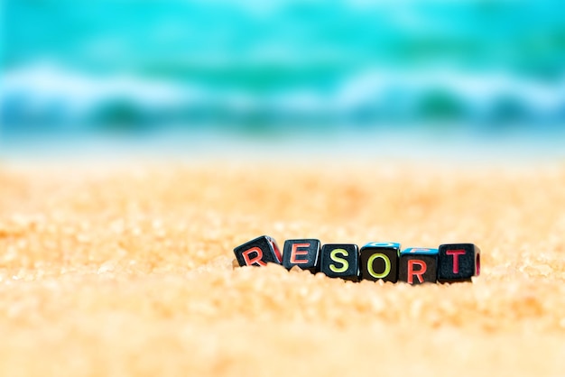 Foto mehrfarbiges wort resort aus schwarzen würfeln im sand auf dem hintergrund von strand und meer