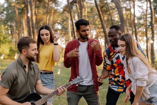 Mehrrassige Gruppe von bärtigen Hipstermännern, die Gitarre spielen, und Freunde, die tanzen und singen