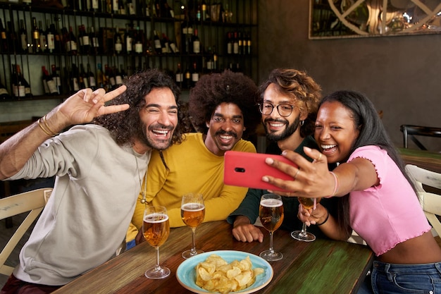 Mehrrassige Versammlung von Freunden, die in einer Bar feiern und Spaß haben, während sie ein Selfie machen