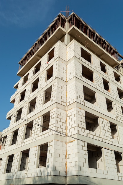 Mehrstöckiges Wohngebäude im Bau und Kran auf einem Hintergrund des blauen Himmels