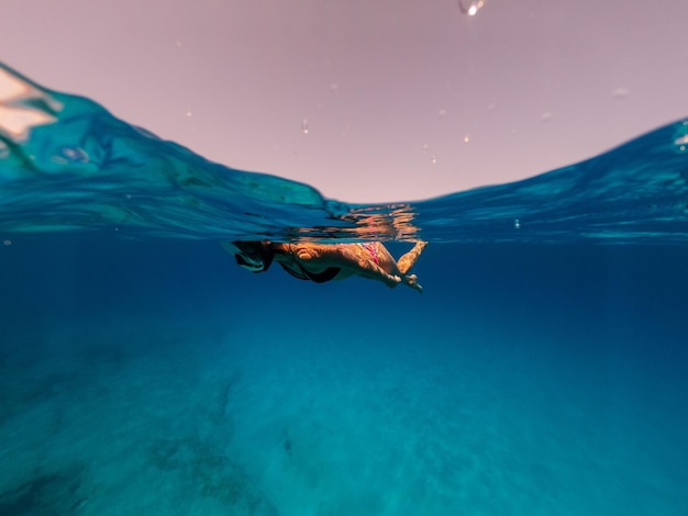 Meia foto subaquática de mulher mergulhando em água cristalina