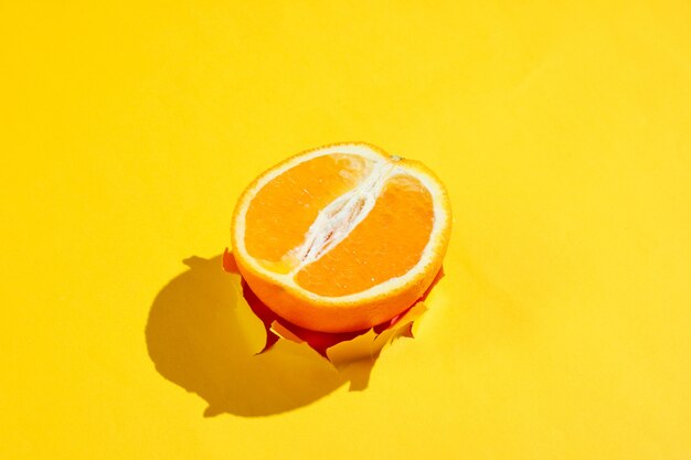 Meia laranja através do furo rasgado no papel amarelo. Conceito de fruta minimalista