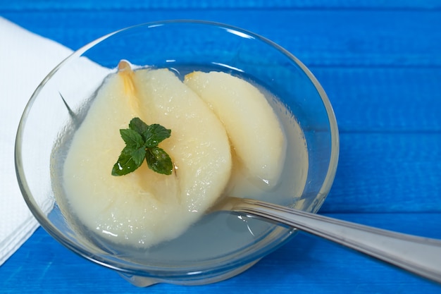 Meia pêra fresca servida com calda doce e folhas de hortelã. fundo azul.