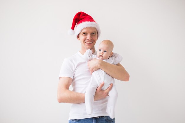 Mein erstes Weihnachten. Papa in Nikolausmütze hält seine kleine Tochter auf weißem Hintergrund mit Kopierraum