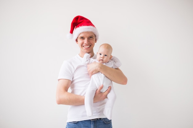 Mein erstes Weihnachten. Papa in Weihnachtsmütze hält seine kleine Tochter auf weißem Hintergrund