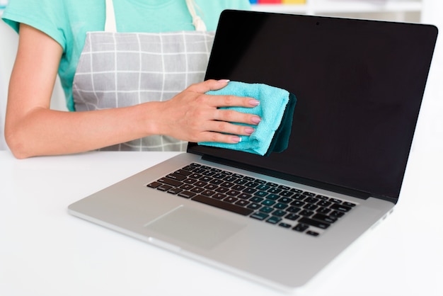 Foto meio de mulher em avental cinza, limpar a tela do laptop em casa