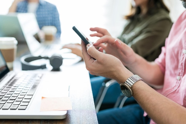 Meio do empresário usando smartphone enquanto trabalhava no laptop por colegas no escritório