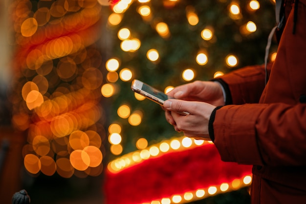 Meio do homem que usa o telefone inteligente contra a árvore de natal iluminada.