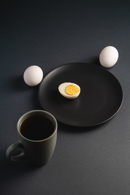 Meio ovo cozido com gema em chapa preta perto de ovos brancos e xícara de chá no escuro