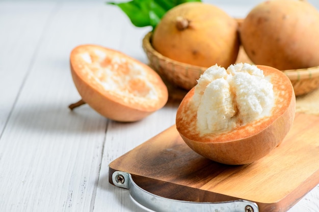 Meio Santol em placa de madeira e fundo de madeira branca Santol tem sabor azedo