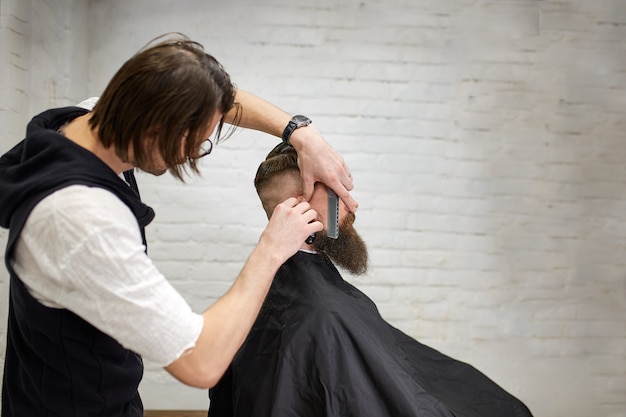 Meister schneidet Haare und Bart von Männern im Friseursalon, Friseur macht Frisur für einen jungen Mann