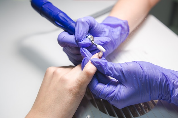 Meister verwenden elektrische Nagelfeilenbohrmaschine im Schönheitssalon. Maniküre-Konzept. Handpflege im Spa