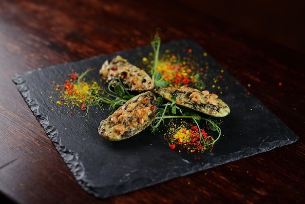 Mejillones al horno con queso y piñones. en un tablero negro