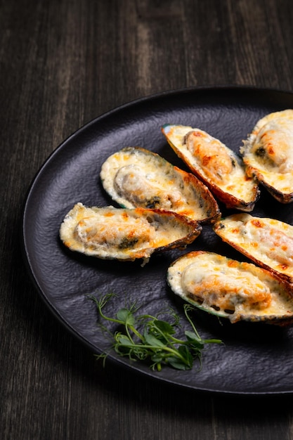 Mejillones al horno con queso en un plato oscuro con hierbas y limón sobre un fondo de madera