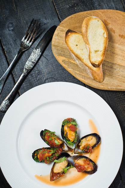 Mejillones al horno en salsa de tomate con cilantro y queso parmesano en un plato blanco.