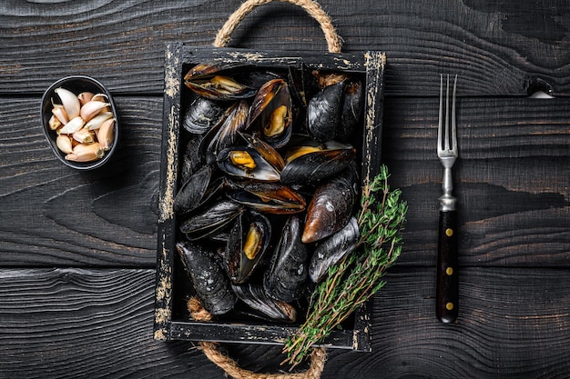 Mejillones al vapor en concha en bandeja de madera con hierbas. Fondo de madera negra. Vista superior.