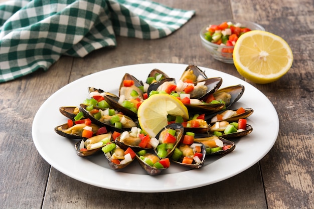 Foto mejillones al vapor con pimientos y cebolla en mesa de madera