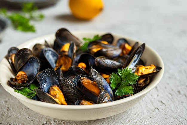 Mejillones al vapor en salsa de vino blanco en un plato blanco, limón y perejil sobre un fondo claro