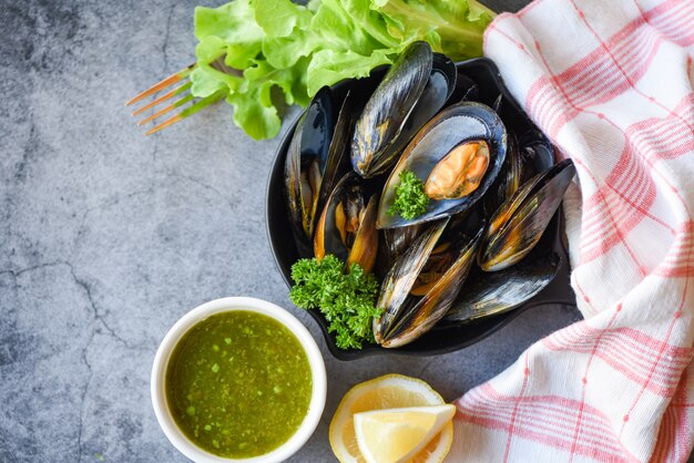 Mejillones cocidos con hierbas limón y fondo de placa oscura - mariscos frescos mariscos en un tazón y ensalada de salsa picante en el restaurante de mejillones