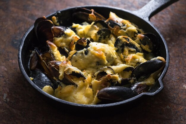 Mejillones cocidos en una sartén de hierro fundido con salsa de queso