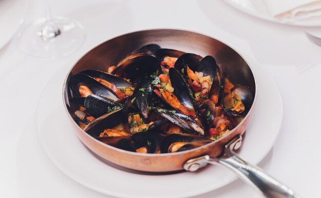 Mejillones hervidos en el plato de cocinar de cobre en el cierre blanco del fondo para arriba.