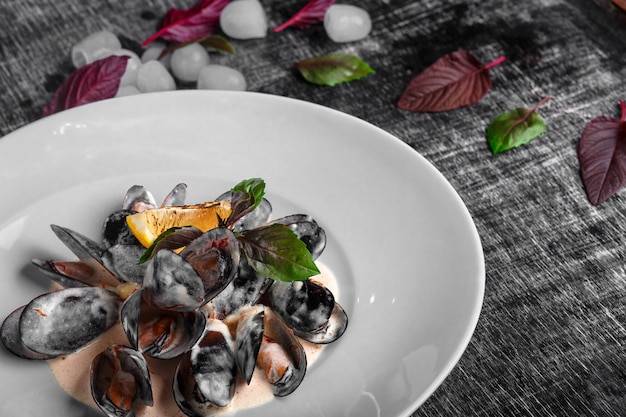 Mejillones de marisco en salsa de crema con limón y albahaca sobre una pizarra negra