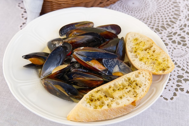 Mejillones con pan blanco en un plato blanco.