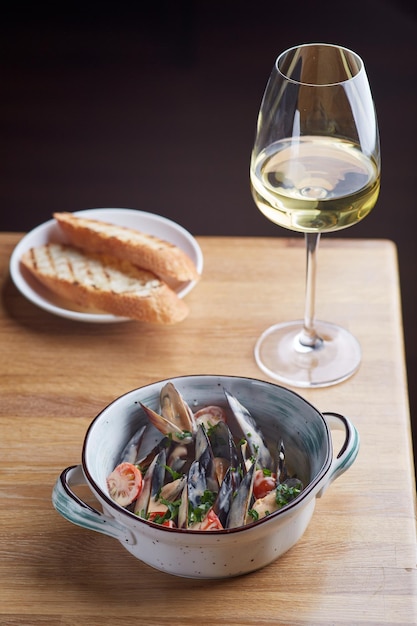 Mejillones con pan a la parrilla y una copa de vino blanco sobre una mesa de madera sabroso concepto de marisco con fondo oscuro