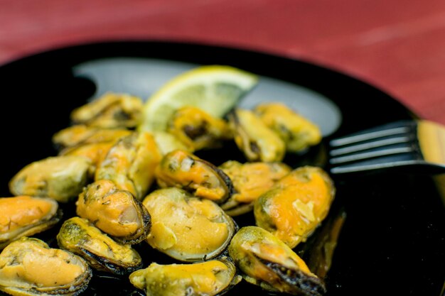 Mejillones en un plato negro sobre un fondo rojo oscuro de madera