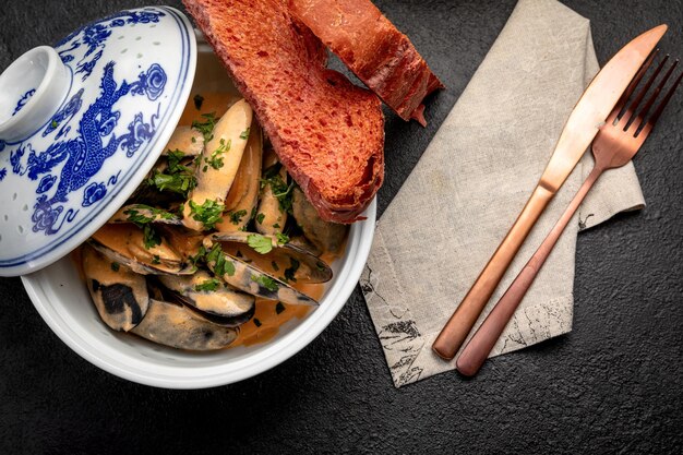 Mejillones en salsa en un plato de cerámica sobre un fondo oscuro decorado