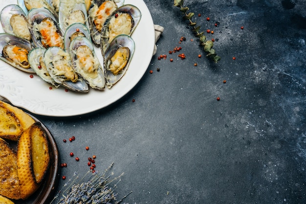 Mejillones verdes al horno con picatostes de parmesano y ajo en una placa blanca.