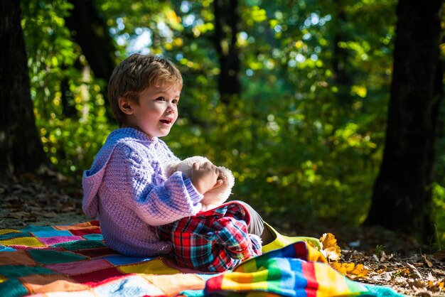 Mejor juntos. Infancia feliz. Inseparable con juguete. Niño lindo jugar con fondo de bosque de juguete de oso de peluche. El niño llevó su juguete favorito a la naturaleza. Picnic con osito de peluche. Senderismo con su juguete favorito