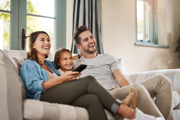 Foto mejor que el cine foto de una joven familia feliz relajándose en el sofá y viendo la televisión juntos en casa