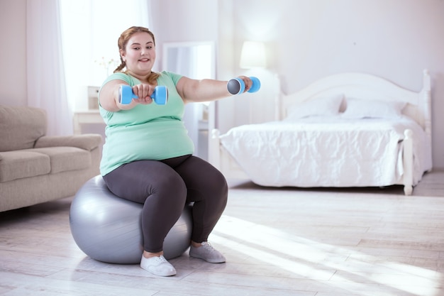 Mejora de la salud. Mujer regordeta inspirada mejorando su salud mientras hace ejercicios con la pelota