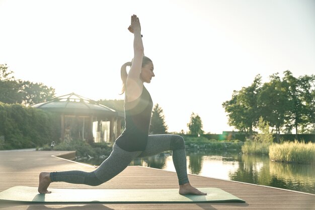 Mejore la toma de cuerpo entero de una mujer relajada de pie en pose de yoga mientras hace yoga en una colchoneta