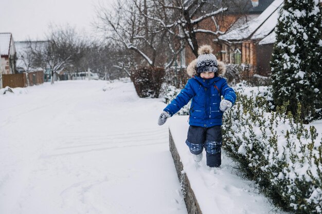 Las mejores actividades de invierno al aire libre para niños niño lindo niño con chaqueta de invierno azul jugando bolas de nieve en