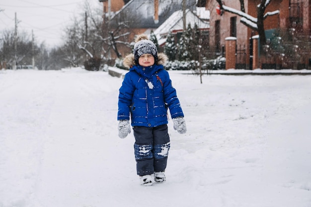 Las mejores actividades de invierno al aire libre para niños niño lindo niño con chaqueta de invierno azul jugando bolas de nieve en