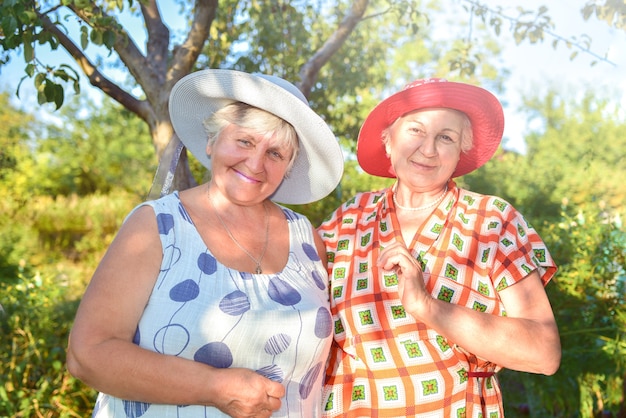 Las mejores amigas jubiladas con sombreros caminan felices en el jardín