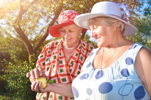 Las mejores amigas jubiladas con sombreros caminan felices en el jardín