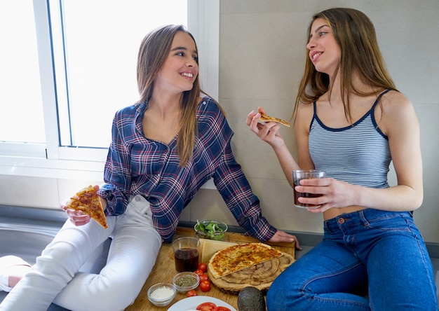 Las mejores amigas que comen pizza en la cocina.