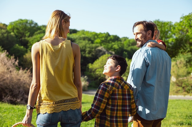 Mejores padres. Alegre muchacho de pelo oscuro caminando con sus padres y su hermana y sonriendo