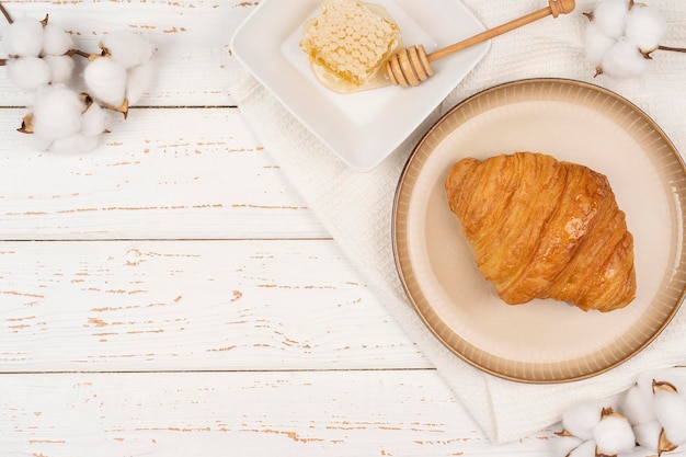 Foto mel com croissants no café da manhã na mesa de madeira branca com caixas de algodão, planta refeição do café da manhã