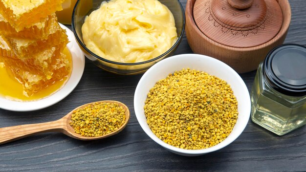 Mel de flores frescas de diferentes variedades, pólen e favo de mel com colheres em um fundo de madeira. vitamina orgânica, comida saudável