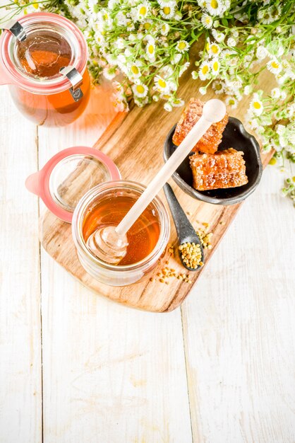 Mel floral orgânico, em frascos, com pentes de pólen e mel, em uma mesa de madeira branca, com flores silvestres