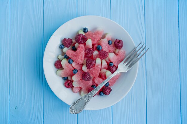 Foto melancia em forma de corações, framboesas, mirtilos em um prato branco. espaço para texto. lanche de frutas. conceito de amor para dia dos namorados.